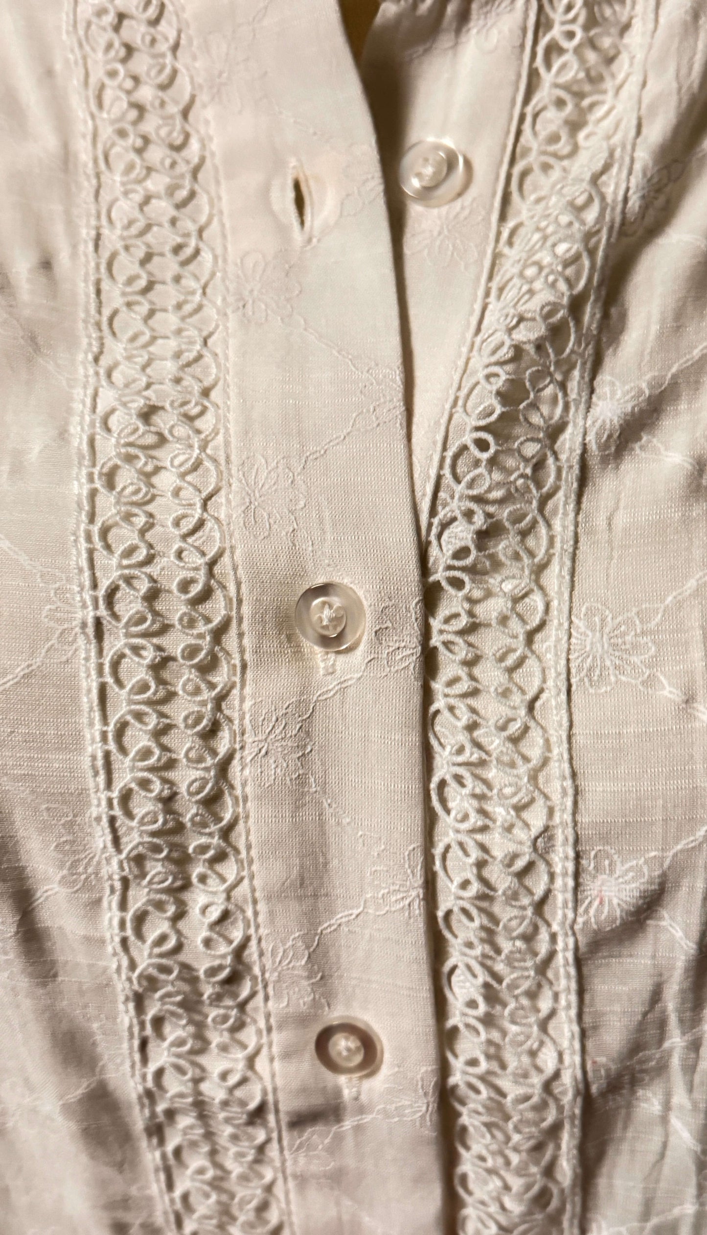 Close-up of a white blouse with button-up design and intricate lace detailing on placket.