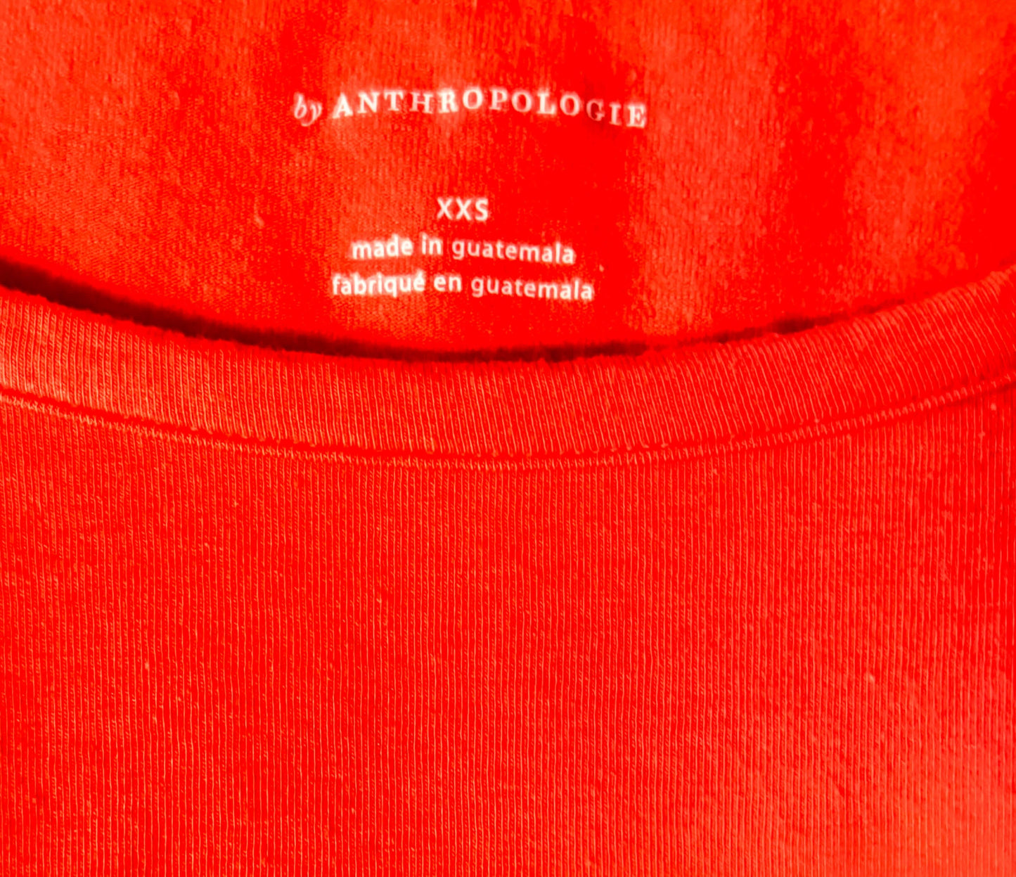Close-up of a red garment with 'by Anthropologie' label on a red background
