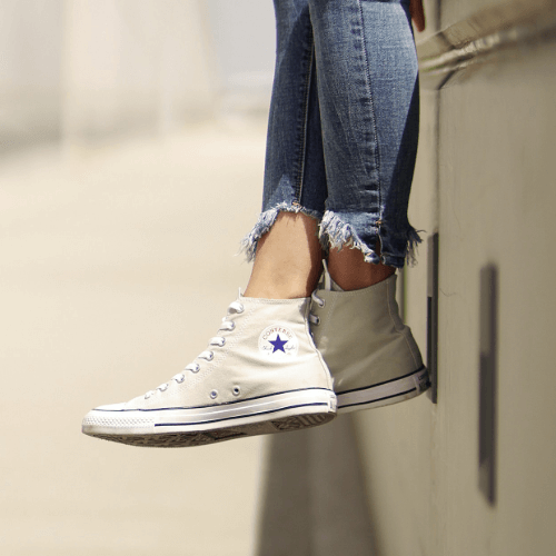 Chuck Taylor Converse All Star High-tops in beige worn by a person sitting on a ledge, showcasing casual street style.