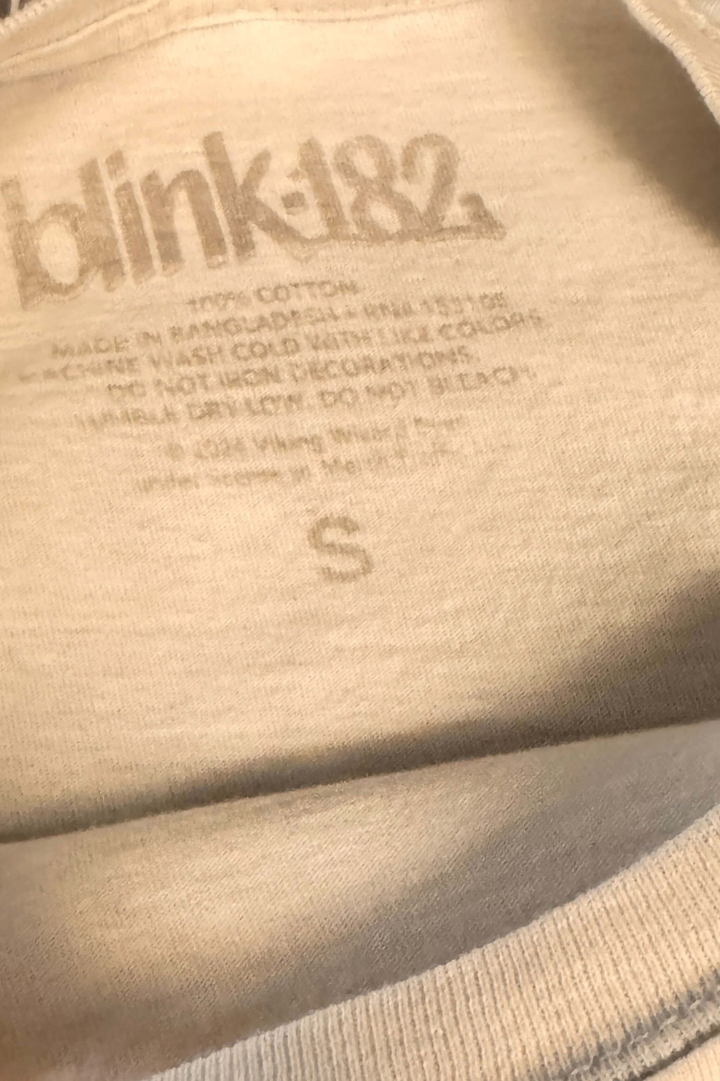 Close-up of off white 'blink-182' tshirt branding and care instructions.