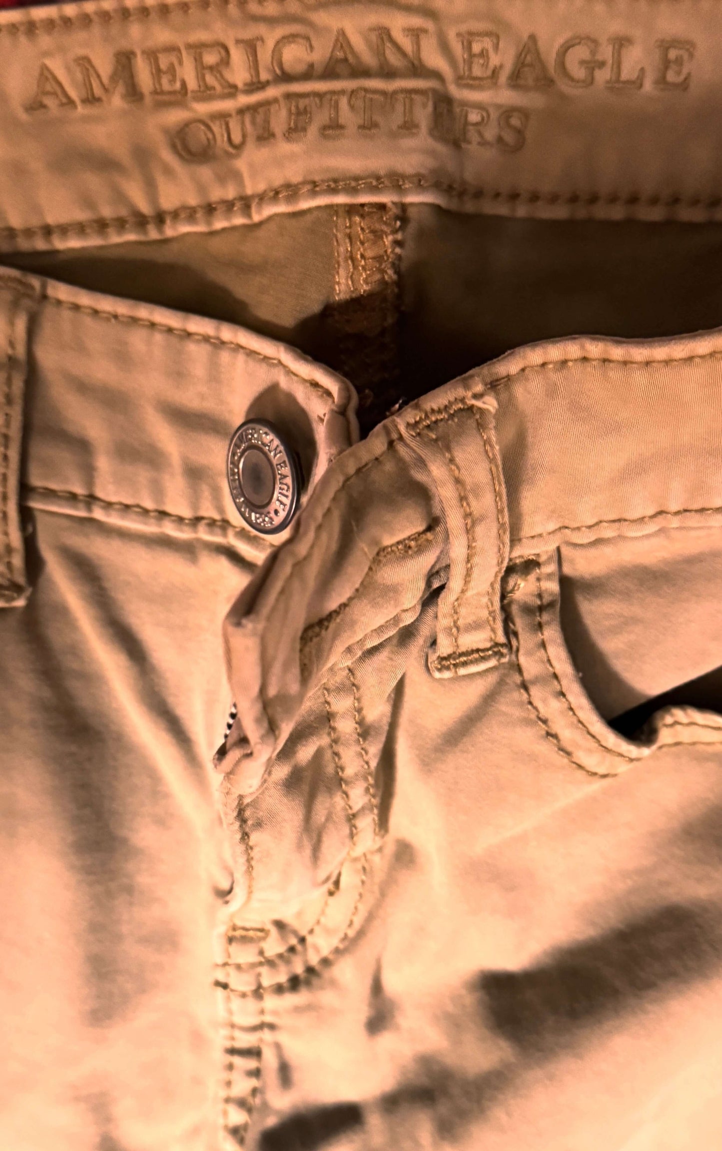Close-up of American Eagle tan denim pants showcasing the button and stitching details, size 4 petite.