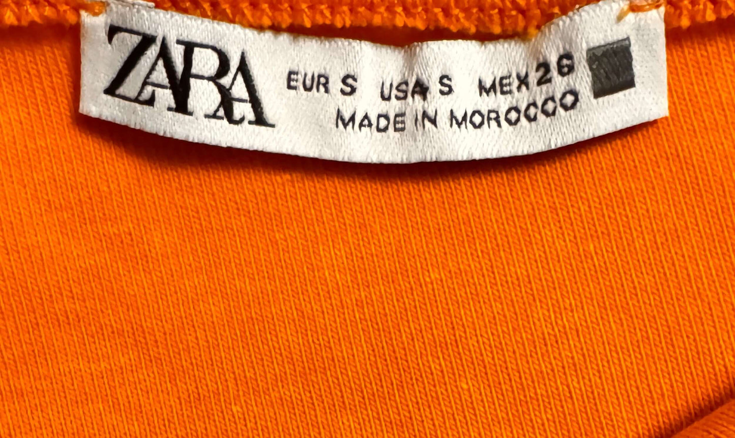 Zara clothing tag showing size small petite and made in Morocco on an orange fabric background.